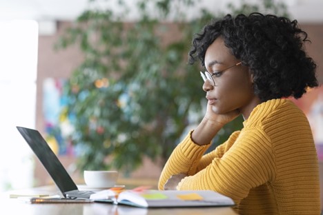 A woman looks at a laptop screen with books next to her